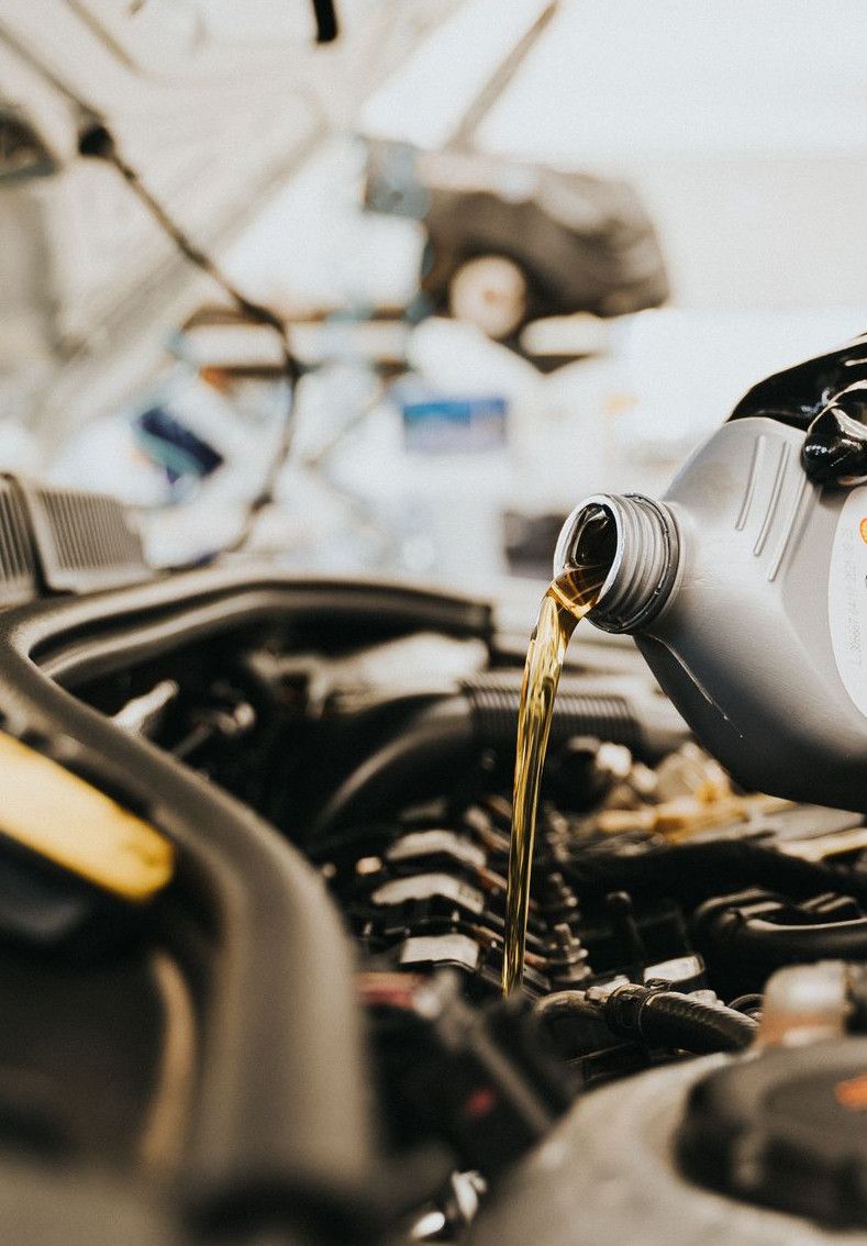 Close-up of a mechanic pouring engine oil into a car engine in an auto repair shop.